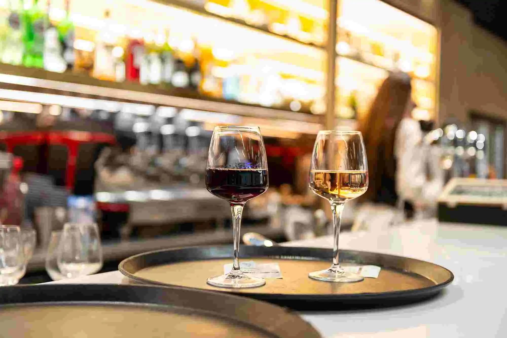 Deux verres de vin, rouge et blanc, posés sur un plateau au comptoir d’un bar.